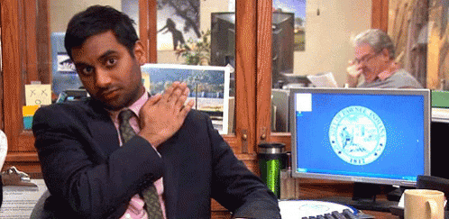 A Man In A Suit And Tie Is Sitting At A Desk In Front Of A Computer With A Seal On It GIF