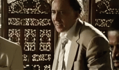 A Man In A Suit And Tie Is Sitting At A Desk In Front Of A Screen . GIF