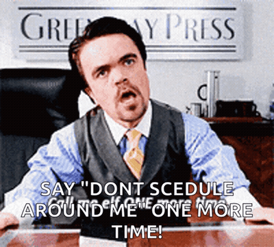 A Man In A Suit And Tie Is Sitting At A Desk In Front Of A Sign That Says ' Greenway Press ' GIF
