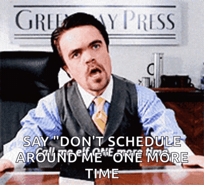 A Man In A Suit And Tie Is Sitting At A Desk In Front Of A Sign That Says " Greenway Press " GIF