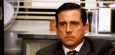 A Man In A Suit And Tie Is Sitting At A Desk In Front Of A Window . GIF