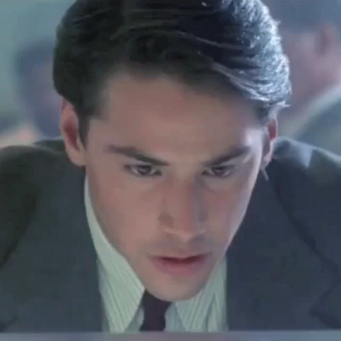 A Man In A Suit And Tie Is Sitting At A Desk Looking At A Computer Screen . GIF