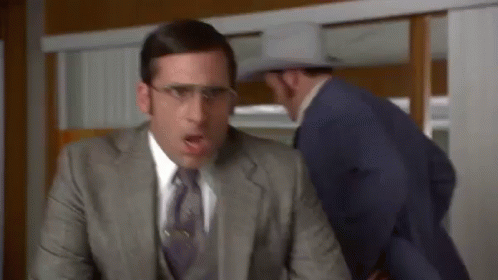 A Man In A Suit And Tie Is Sitting At A Desk While Another Man In A Cowboy Hat Looks On . GIF