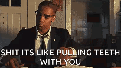 A Man In A Suit And Tie Is Sitting At A Desk With A Book And Glasses On . GIF