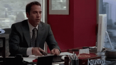 A Man In A Suit And Tie Is Sitting At A Desk With A Box On It That Says Aquafina GIF