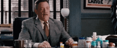 A Man In A Suit And Tie Is Sitting At A Desk With A Bunch Of Pills On It . GIF