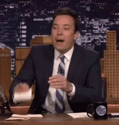 A Man In A Suit And Tie Is Sitting At A Desk With A Cup Of Coffee . GIF