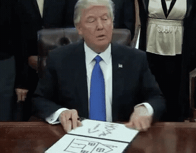 A Man In A Suit And Tie Is Sitting At A Desk With A Drawing Of A House On A Piece Of Paper . GIF