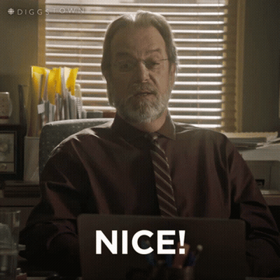 A Man In A Suit And Tie Is Sitting At A Desk With A Laptop And Says Nice GIF