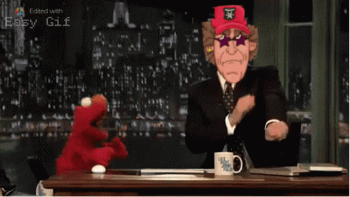A Man In A Suit And Tie Is Sitting At A Desk With A Mug That Says Let 'S Get This Talk On It GIF