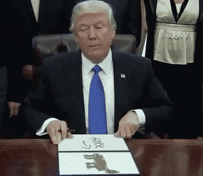 A Man In A Suit And Tie Is Sitting At A Desk With A Piece Of Paper That Says ' Trump ' On It GIF