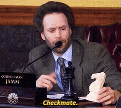 A Man In A Suit And Tie Is Sitting At A Desk With A Sign That Says Checkmate GIF