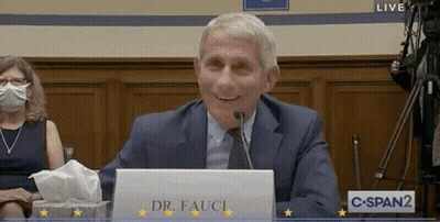 A Man In A Suit And Tie Is Sitting At A Desk With A Sign That Says Dr. Fauci GIF