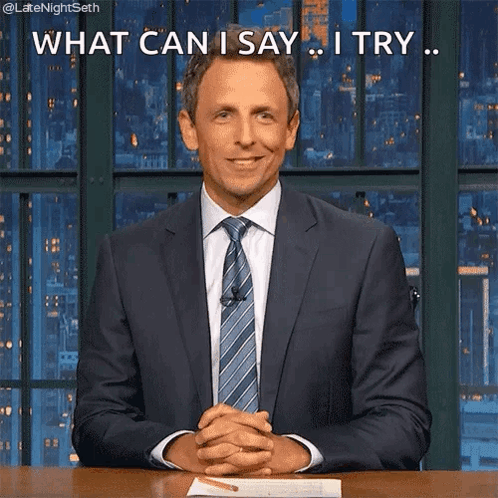 A Man In A Suit And Tie Is Sitting At A Desk With His Hands Folded And Says What Can I Say I Try . GIF