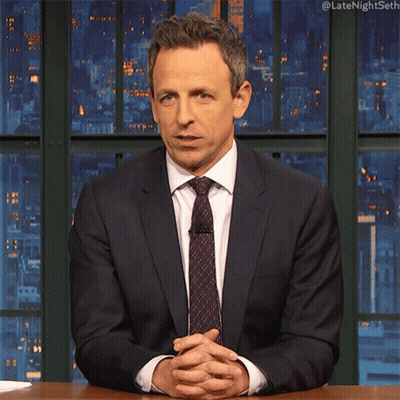 A Man In A Suit And Tie Is Sitting At A Desk With His Hands Folded GIF