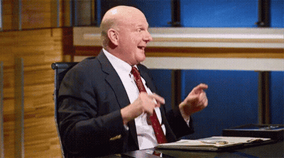 A Man In A Suit And Tie Is Sitting At A Desk With His Hands In The Air . GIF