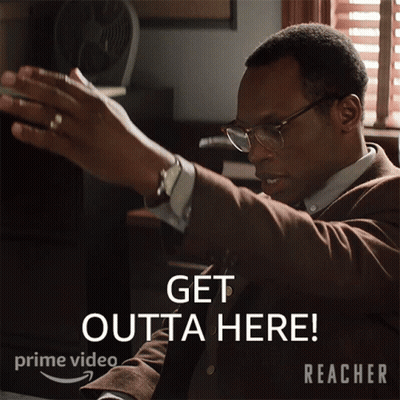 A Man In A Suit And Tie Is Sitting At A Desk With The Words Get Outta Here Written Below Him GIF