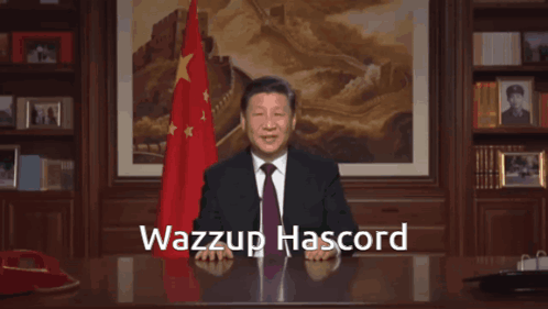 A Man In A Suit And Tie Is Sitting At A Desk With The Words Wazzup Hascord Written On The Top GIF