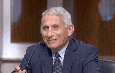 A Man In A Suit And Tie Is Sitting At A Microphone And Smiling . GIF