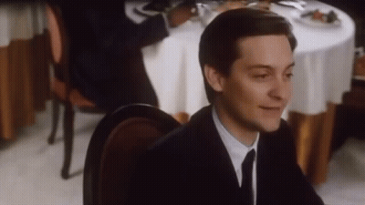 A Man In A Suit And Tie Is Sitting At A Restaurant Table . GIF