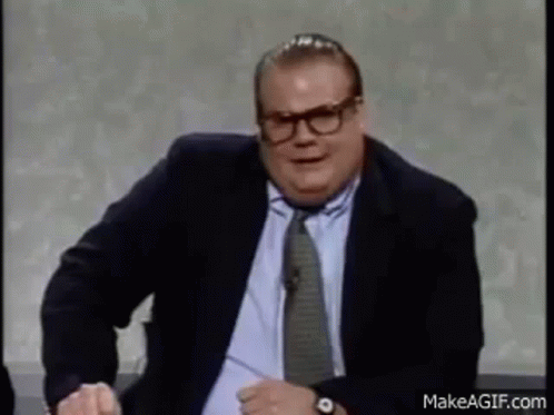 A Man In A Suit And Tie Is Sitting At A Table And Making A Funny Face . GIF