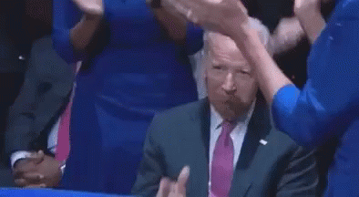 A Man In A Suit And Tie Is Sitting At A Table And Pointing At Something . GIF