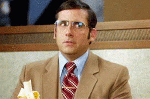 A Man In A Suit And Tie Is Sitting At A Table Eating A Banana GIF