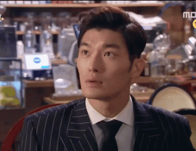 A Man In A Suit And Tie Is Sitting At A Table In Front Of A Sign That Says Md GIF