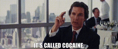 A Man In A Suit And Tie Is Sitting At A Table In Front Of A Window And Holding A Piece Of Chocolate . GIF