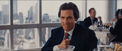 A Man In A Suit And Tie Is Sitting At A Table In Front Of A Window GIF
