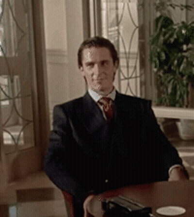A Man In A Suit And Tie Is Sitting At A Table Looking At The Camera GIF