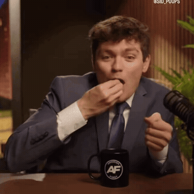 A Man In A Suit And Tie Is Sitting At A Table With A Black Mug That Says American Family GIF
