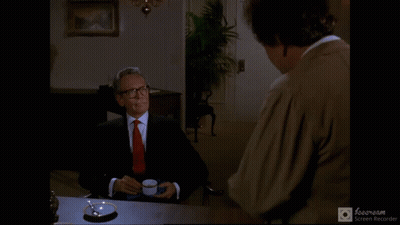 A Man In A Suit And Tie Is Sitting At A Table With A Cup Of Coffee And The Words " C'est Tout " Above Him GIF