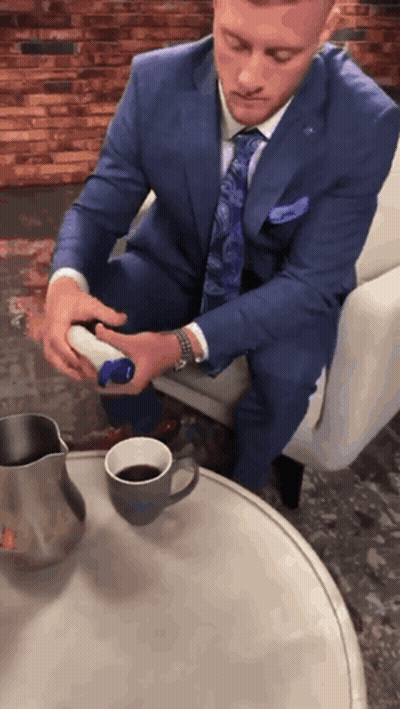A Man In A Suit And Tie Is Sitting At A Table With A Cup Of Coffee On It GIF