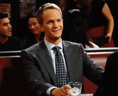 A Man In A Suit And Tie Is Sitting At A Table With A Drink . GIF