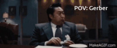 A Man In A Suit And Tie Is Sitting At A Table With A Makeagif.com Link In The Corner GIF