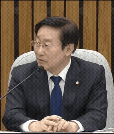 A Man In A Suit And Tie Is Sitting At A Table With A Microphone GIF