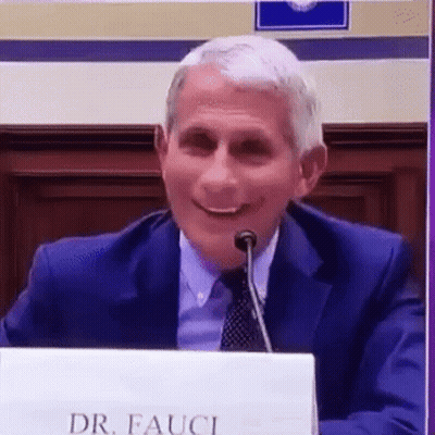 A Man In A Suit And Tie Is Sitting At A Table With A Microphone . GIF