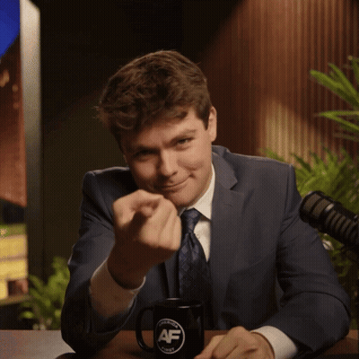 A Man In A Suit And Tie Is Sitting At A Table With A Mug That Says Af GIF