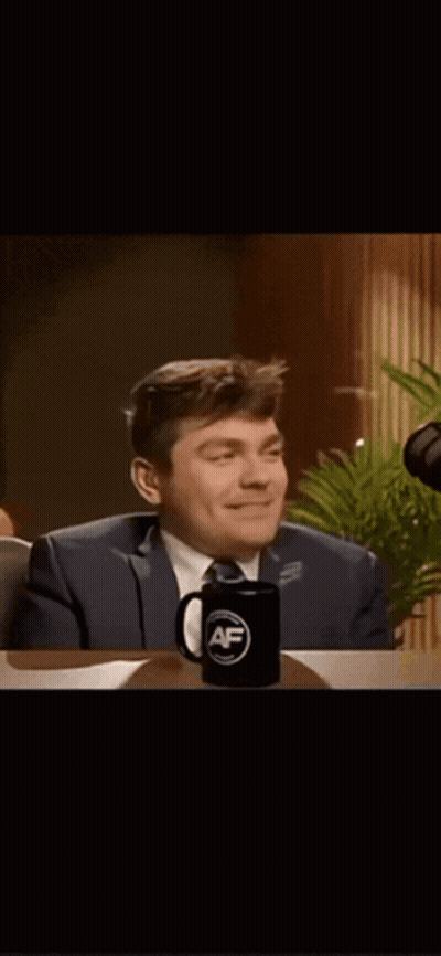 A Man In A Suit And Tie Is Sitting At A Table With A Mug That Says ' Af ' On It GIF