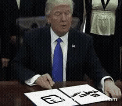 A Man In A Suit And Tie Is Sitting At A Table With A Piece Of Paper That Says ' Donald Trump ' On It GIF