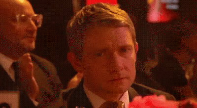 A Man In A Suit And Tie Is Sitting At A Table With A Pink Flower In Front Of Him . GIF