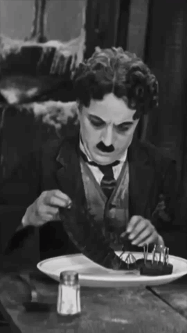 A Man In A Suit And Tie Is Sitting At A Table With A Plate Of Food And A Salt And Pepper Shaker GIF