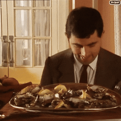 A Man In A Suit And Tie Is Sitting At A Table With A Plate Of Food In Front Of Him That Says Turkey On It GIF