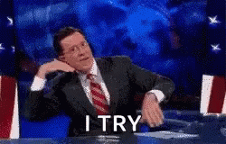 A Man In A Suit And Tie Is Sitting At A Table With A Sign That Says I Try . GIF