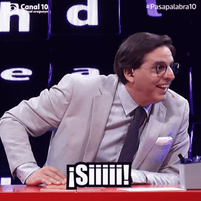 A Man In A Suit And Tie Is Sitting At A Table With A Sign That Says ' Siiiiii ' On It GIF