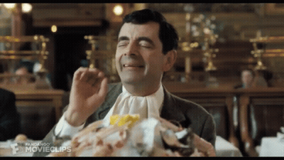 A Man In A Suit And Tie Is Sitting At A Table With His Eyes Closed And A Pile Of Food .. GIF