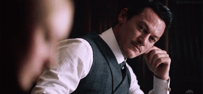 A Man In A Suit And Tie Is Sitting At A Table With His Hands On His Chin . GIF