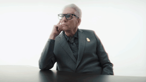 A Man In A Suit And Tie Is Sitting At A Table With The Word Excuse Written On It GIF
