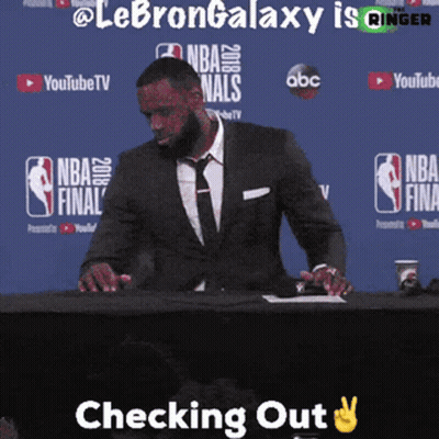 A Man In A Suit And Tie Is Sitting At A Table With The Words Checking Out Above Him GIF